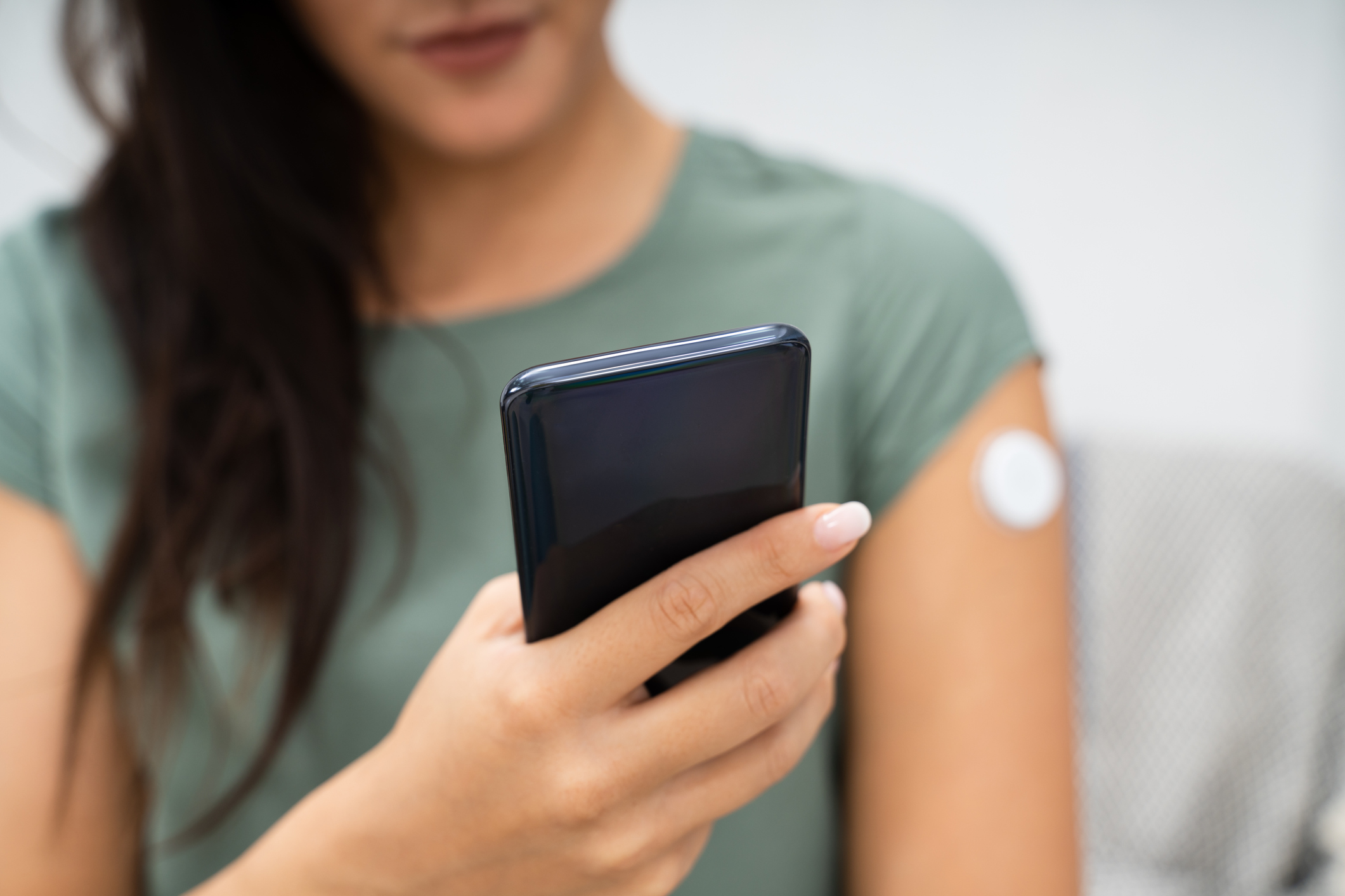 Image shows a woman holding a cellphone while she tracks her blood sugar with her glucose monitor on her arm
